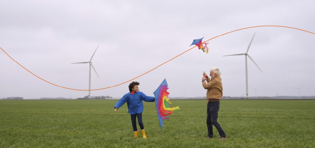 Una niña y un adulto mayor con barriletes frente a molinos de energía eólica, representando el financiamiento sostenible de Rabobank: banco cooperativo.