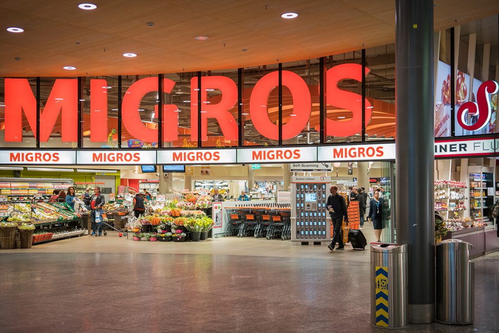 Entrada a un supermercado cooperativo Migros en Suiza, reflejando el consumo asociativo en el marco del partido Argentina vs Suiza.